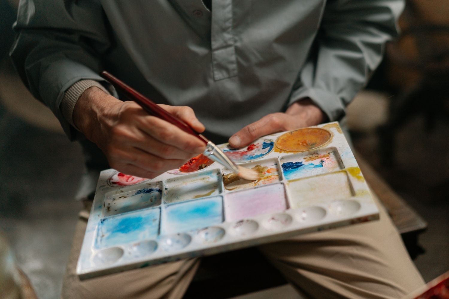 Close-up of an artist's hands mixing colour on a watercolour palette